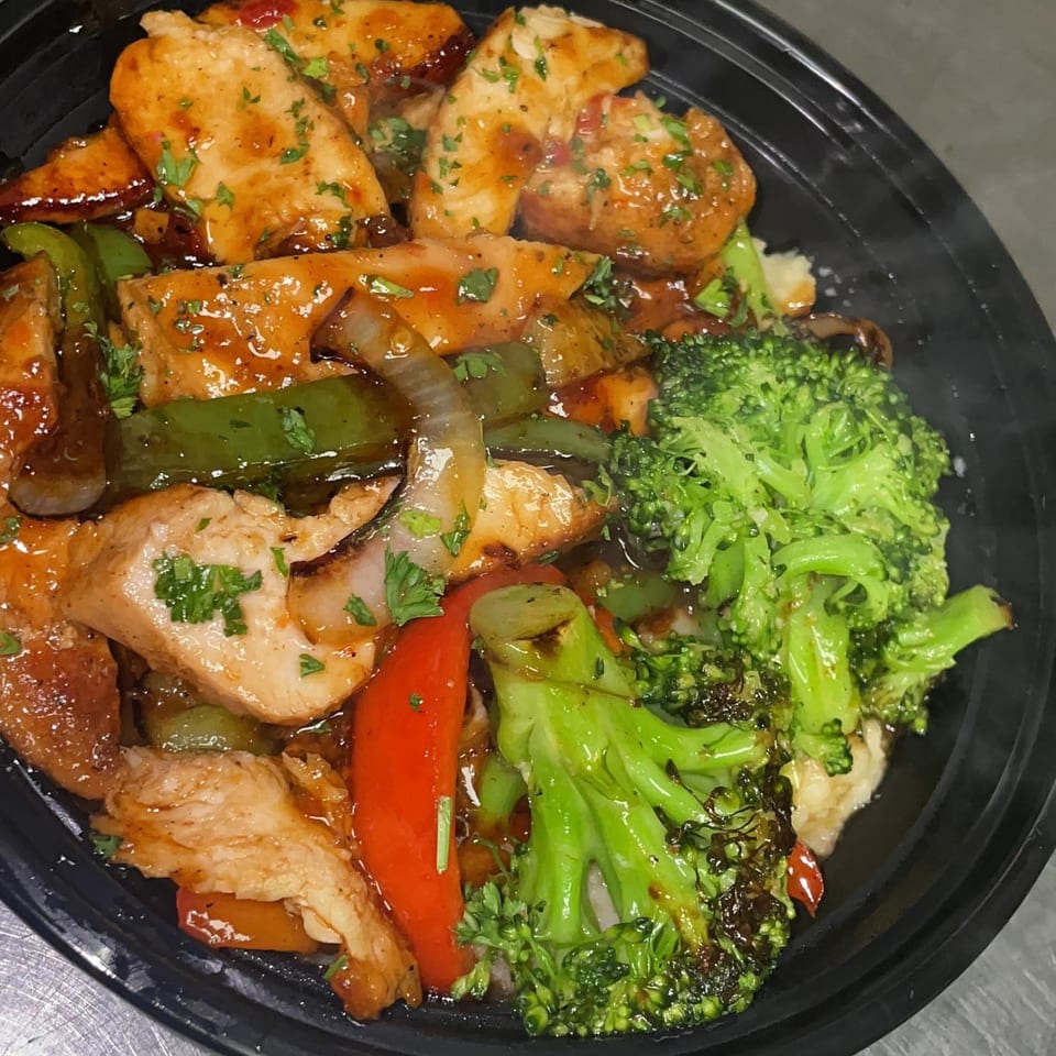 The Flava Zone's Caribbean chicken and broccoli stir-fry with peppers and onions in a black bowl.