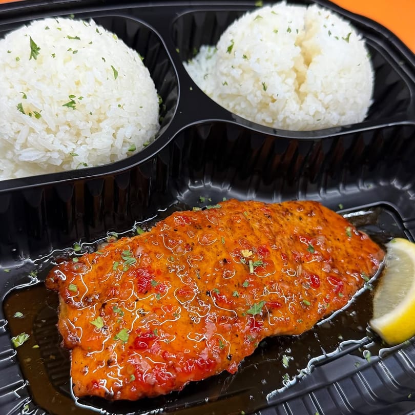 Caribbean salmon with a vibrant orange sauce, garnished with herbs and a lemon wedge, served with white rice.