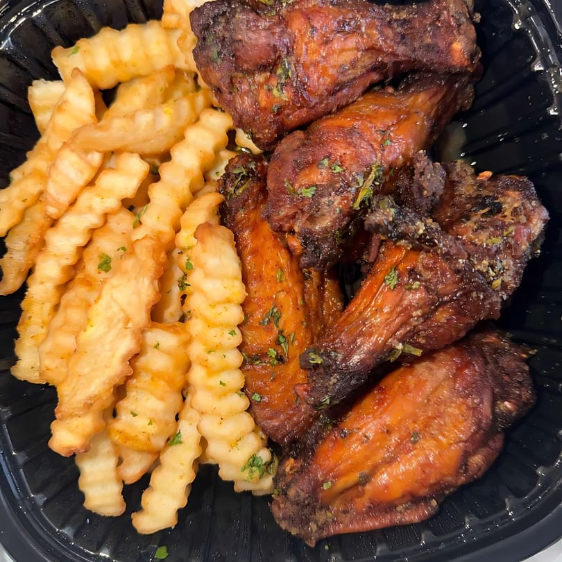 The Flava Zone's jerk chicken wings and crinkle-cut fries in a black takeout container.